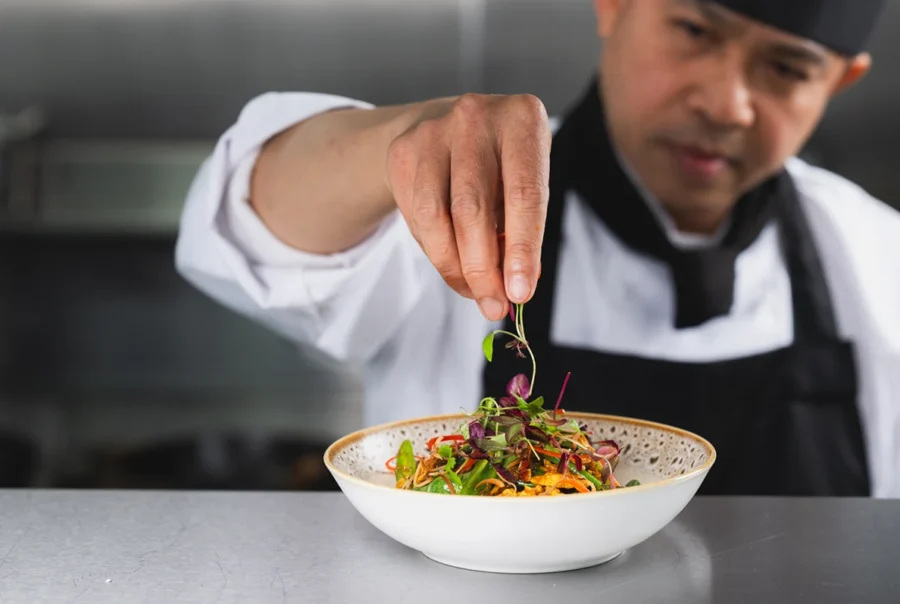 chef adding leaves to a dish of food