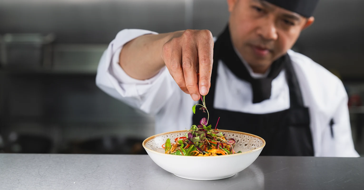 chef adding leaves to a dish of food