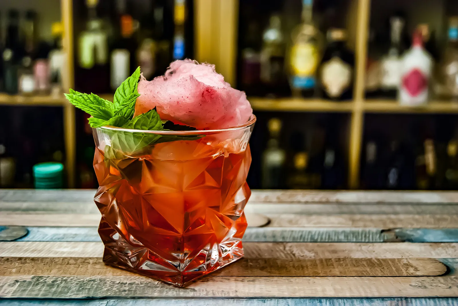 A whiskey cocktail loaded with ice and mint in a geometric glass on a wooden bar